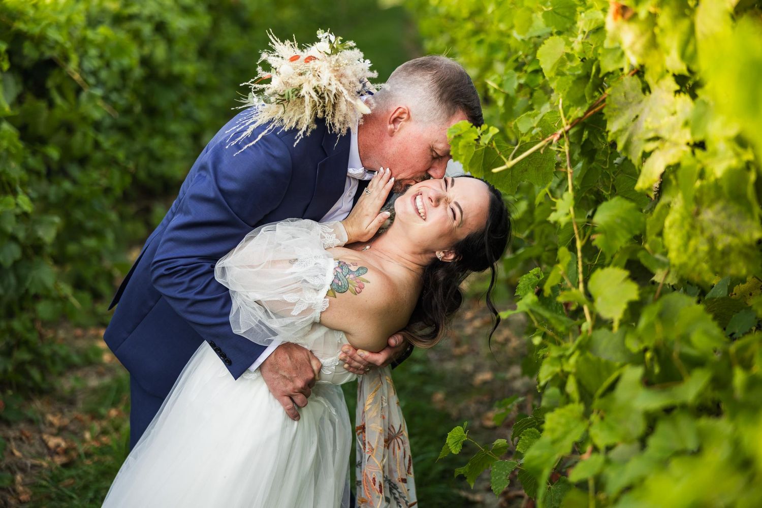 Intimate moment between newlyweds among green vineyard rows.