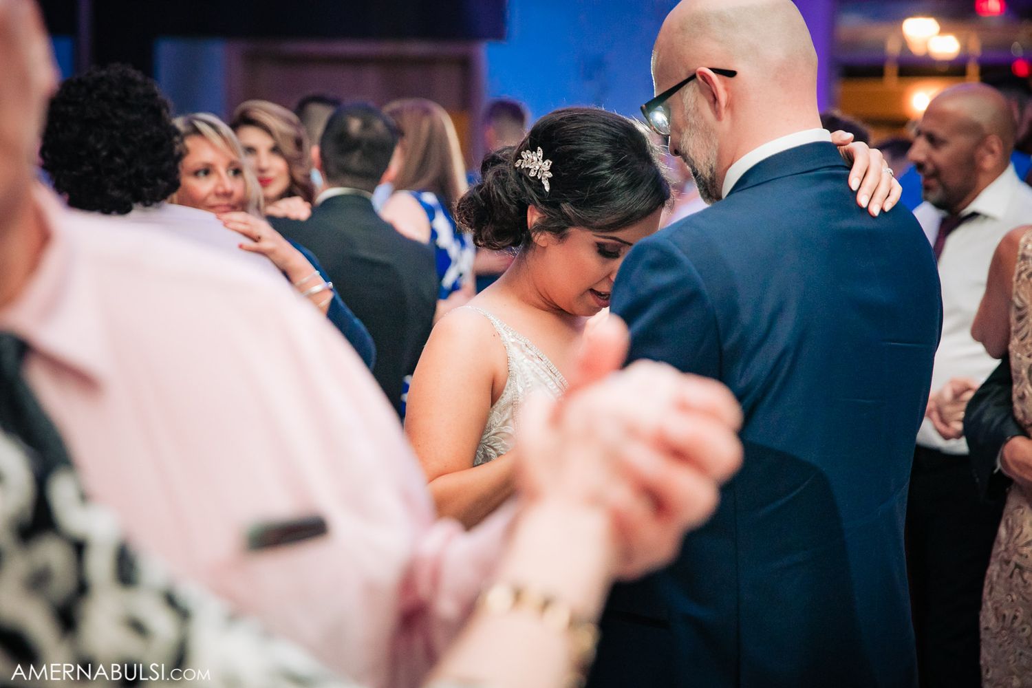 Wedding reception guests dancing and celebrating on a crowded dance floor with purple lighting.