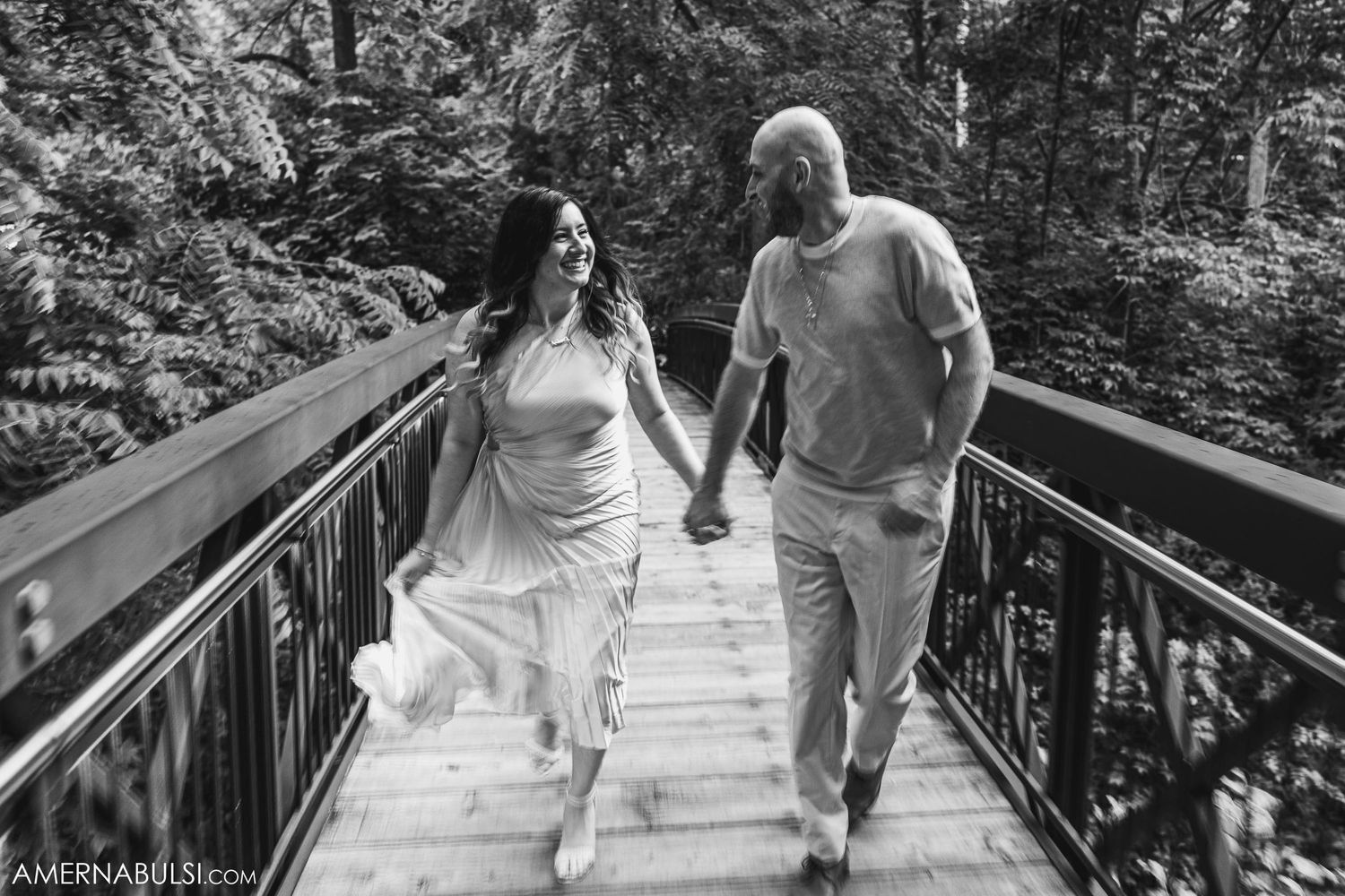 A couple walking hand in hand on a wooden bridge walkway in black and white.
