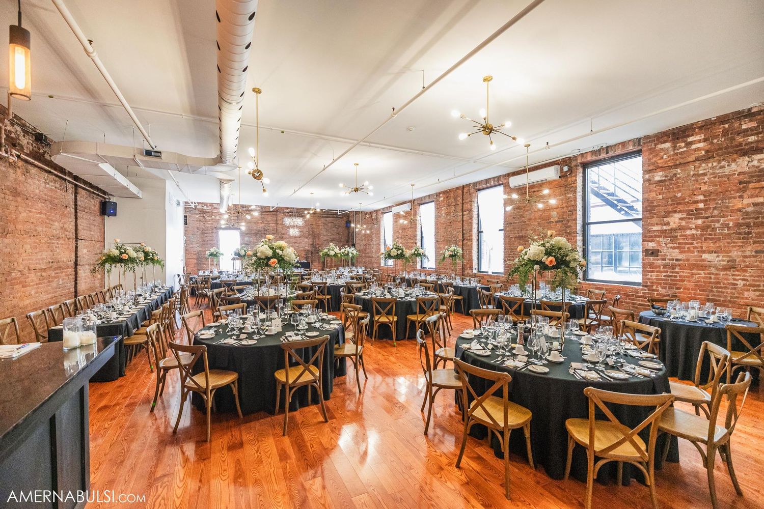 Reception venue with exposed brick walls and round tables decorated in elegant black linens.