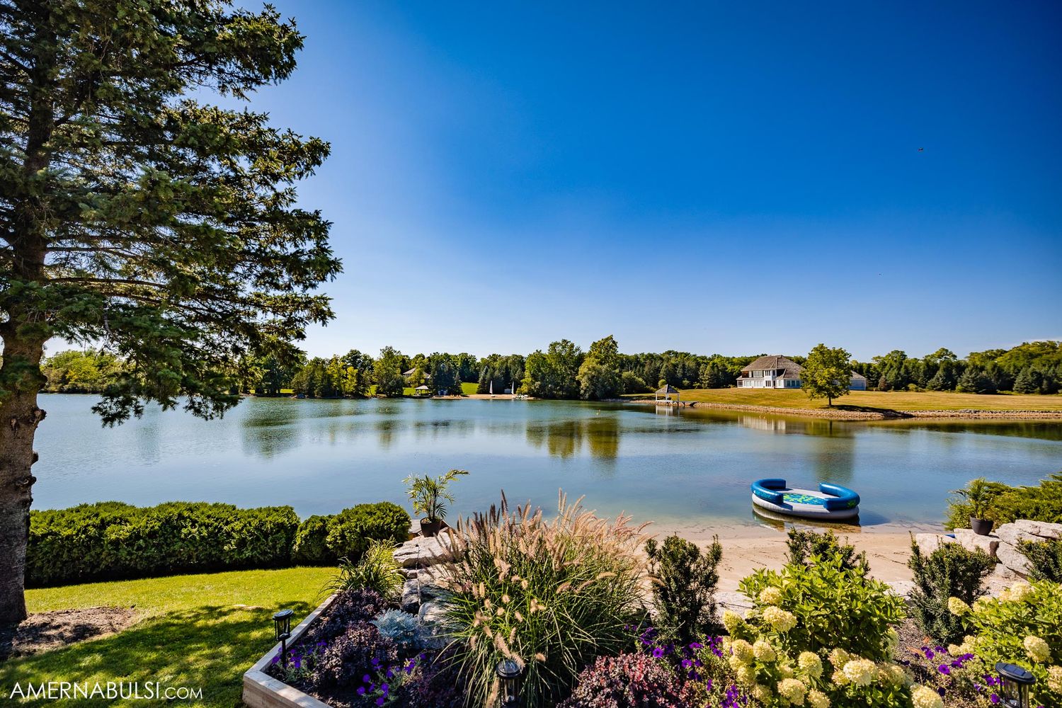 Serene lakeside landscape with trees and flowers on a sunny summer day.