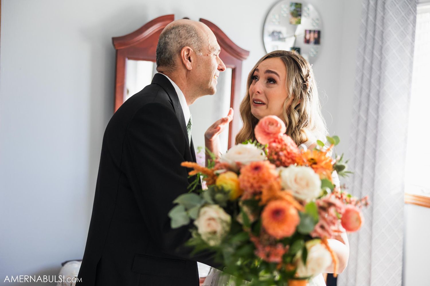An emotional wedding day moment captured indoors with peach and coral floral arrangement.
