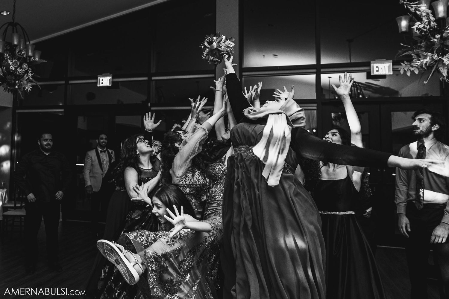 Black and white photo of wedding guests reaching for bouquet toss at reception.