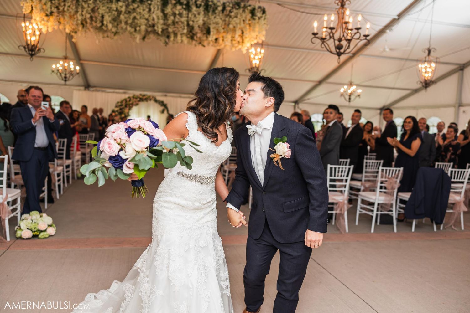 Couple shares romantic moment under floral chandelier during wedding reception.