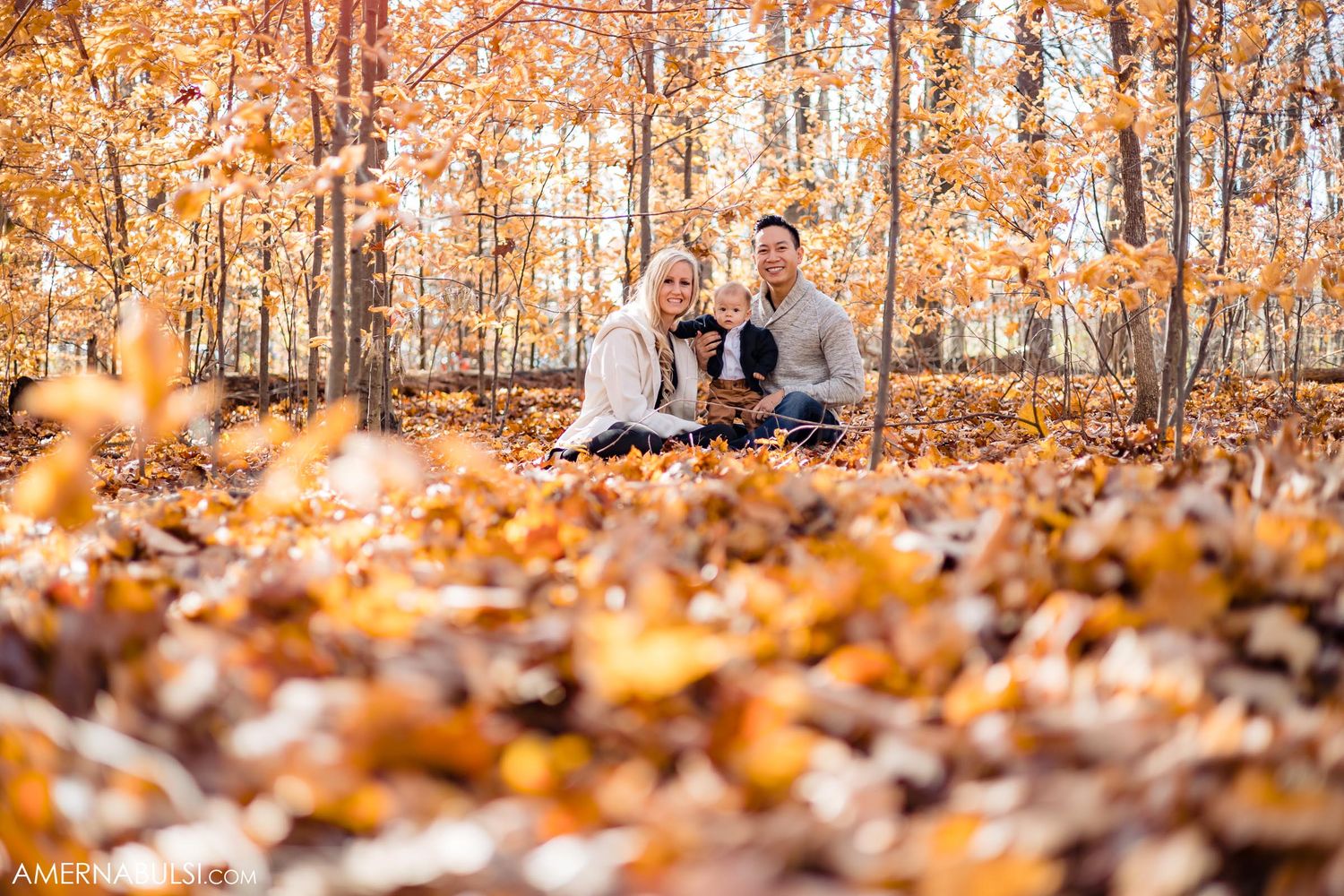 Couple sitting on ground surrounded by vibrant orange fallen autumn leaves in forest.
