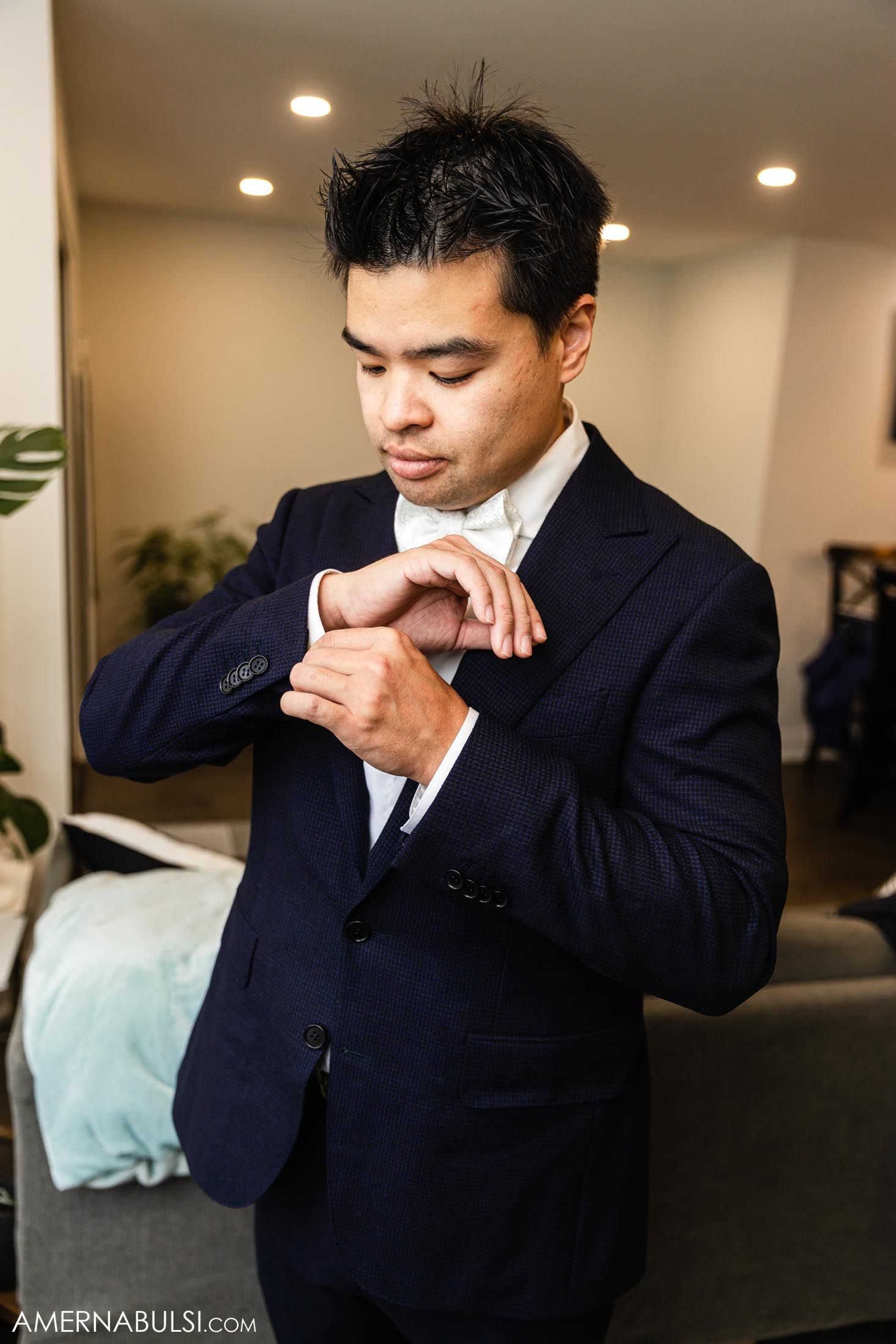 Person in navy suit adjusting cufflinks during wedding preparations.