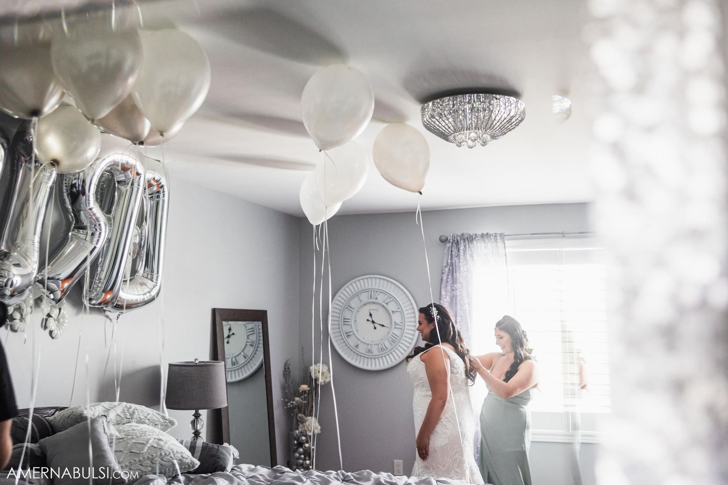 Wedding prep room with white balloons, chandelier, and figures in white and sage green dresses.