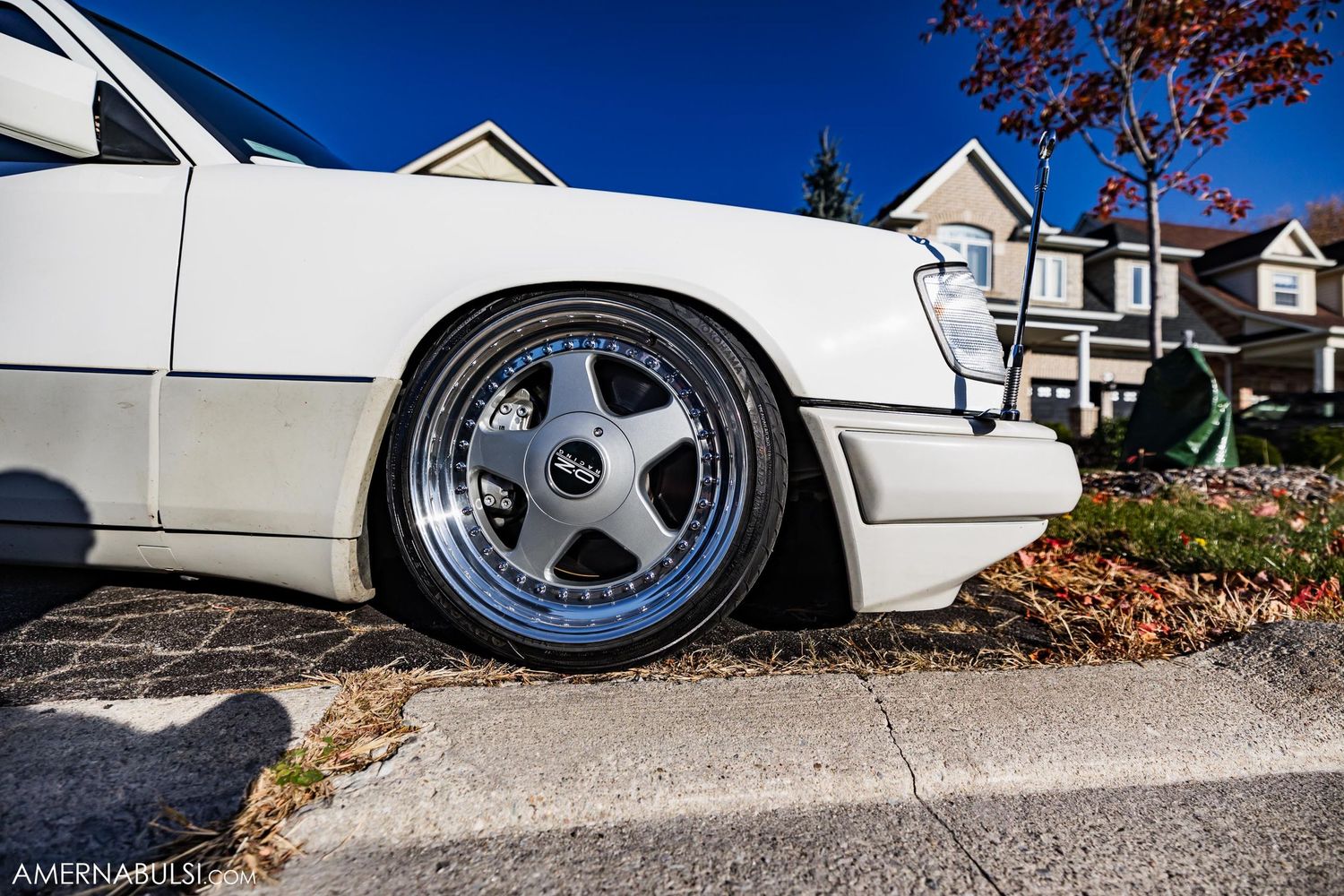 Close-up of a lowered white car with custom chrome five-spoke wheel.