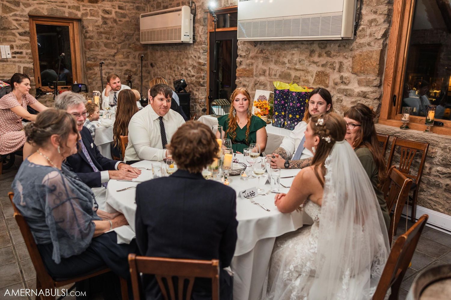 Wedding guests gathered around tables in rustic stone-walled reception venue.