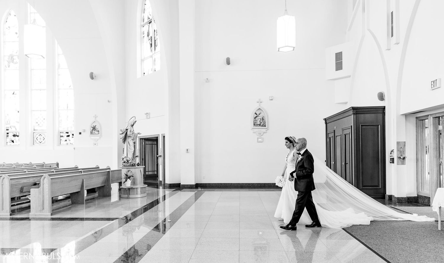 Black and white photo of priest walking through empty church interior.