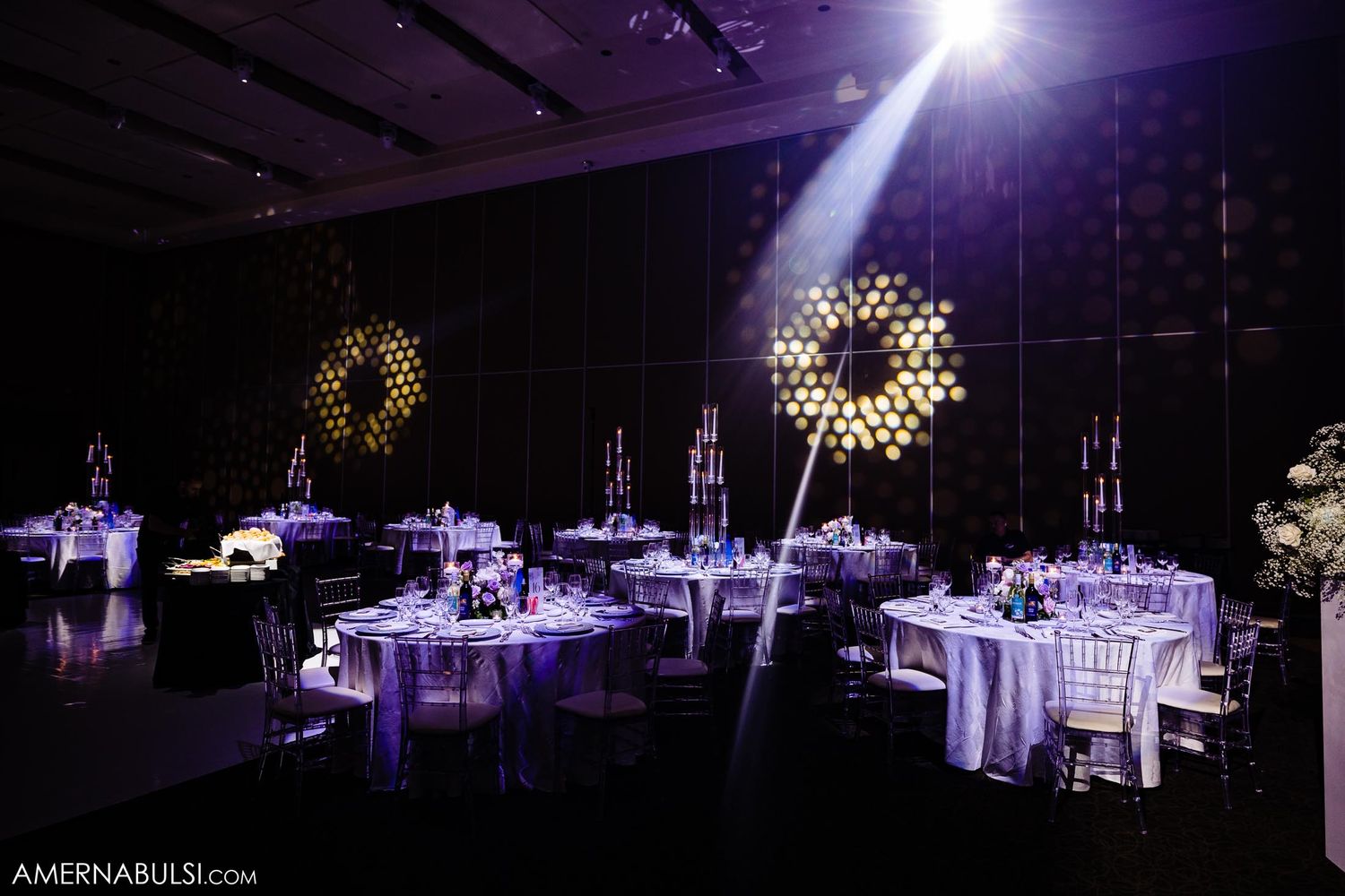Purple-lit wedding reception venue with elegant table settings and dramatic spotlight effect.