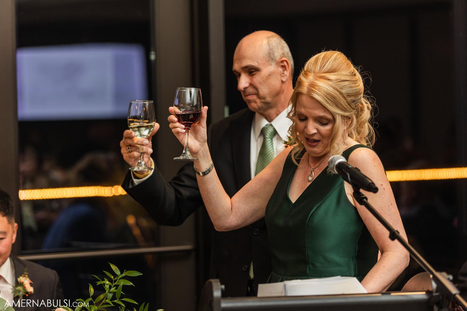 Two guests raise their wine glasses during a formal celebration speech.