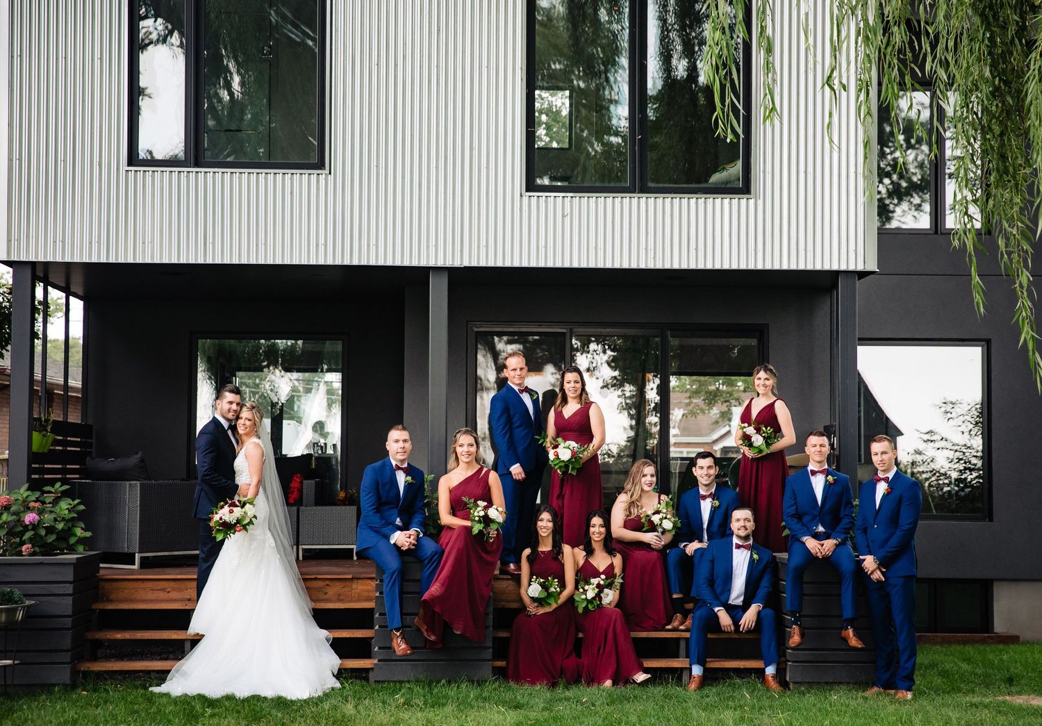 Wedding party in navy and burgundy attire poses casually outside modern building.