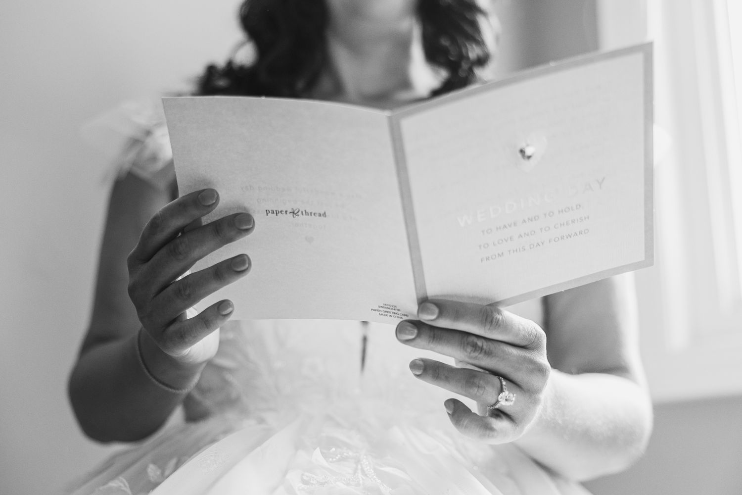 Bride reading a heartfelt wedding card in black and white, wearing a white gown and engagement ring.