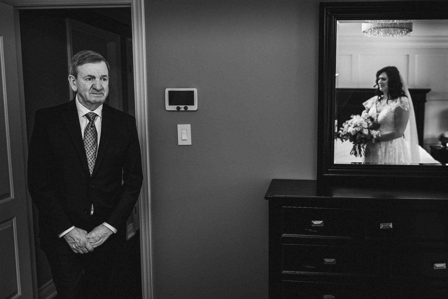Emotional black and white photo of father seeing bride in wedding dress reflected in mirror.