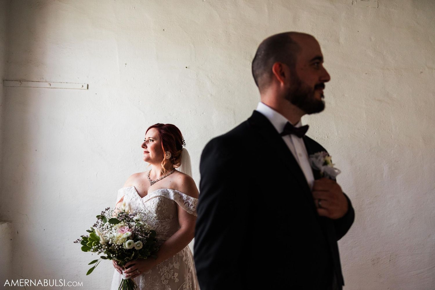 Artistic wedding portrait in minimalist white room with natural light and bridal bouquet.