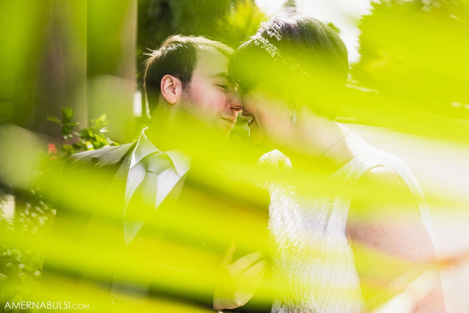 Artistic wedding photo through green foliage with soft focus effect.