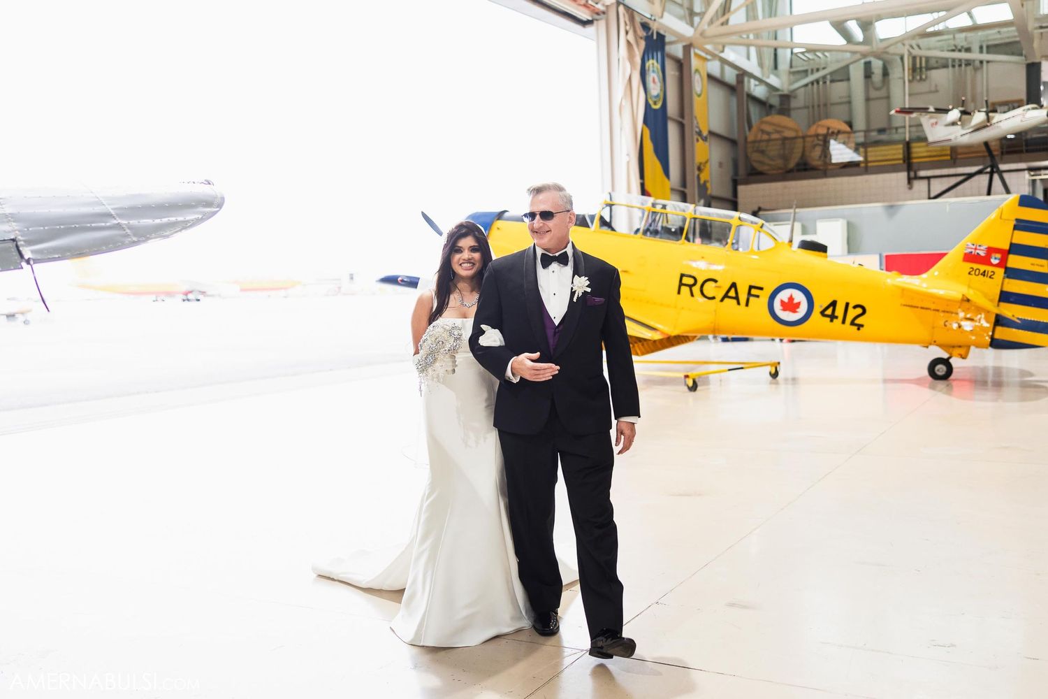 Couple poses in front of yellow vintage aircraft during wedding photoshoot.
