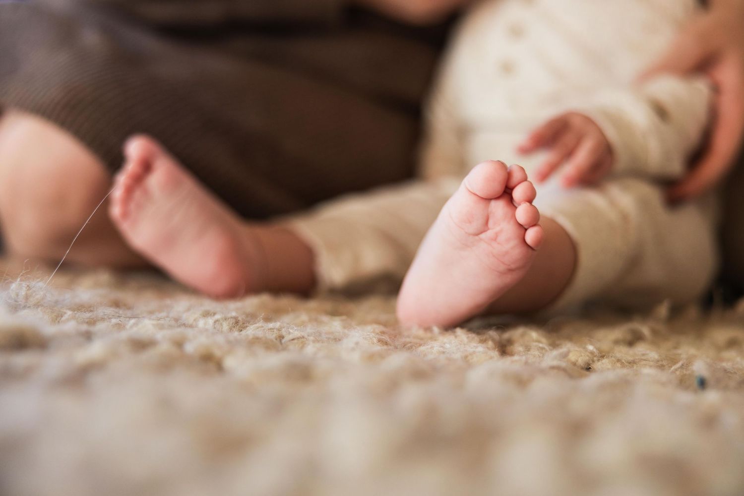 Close-up of tiny baby feet against a soft carpet texture.