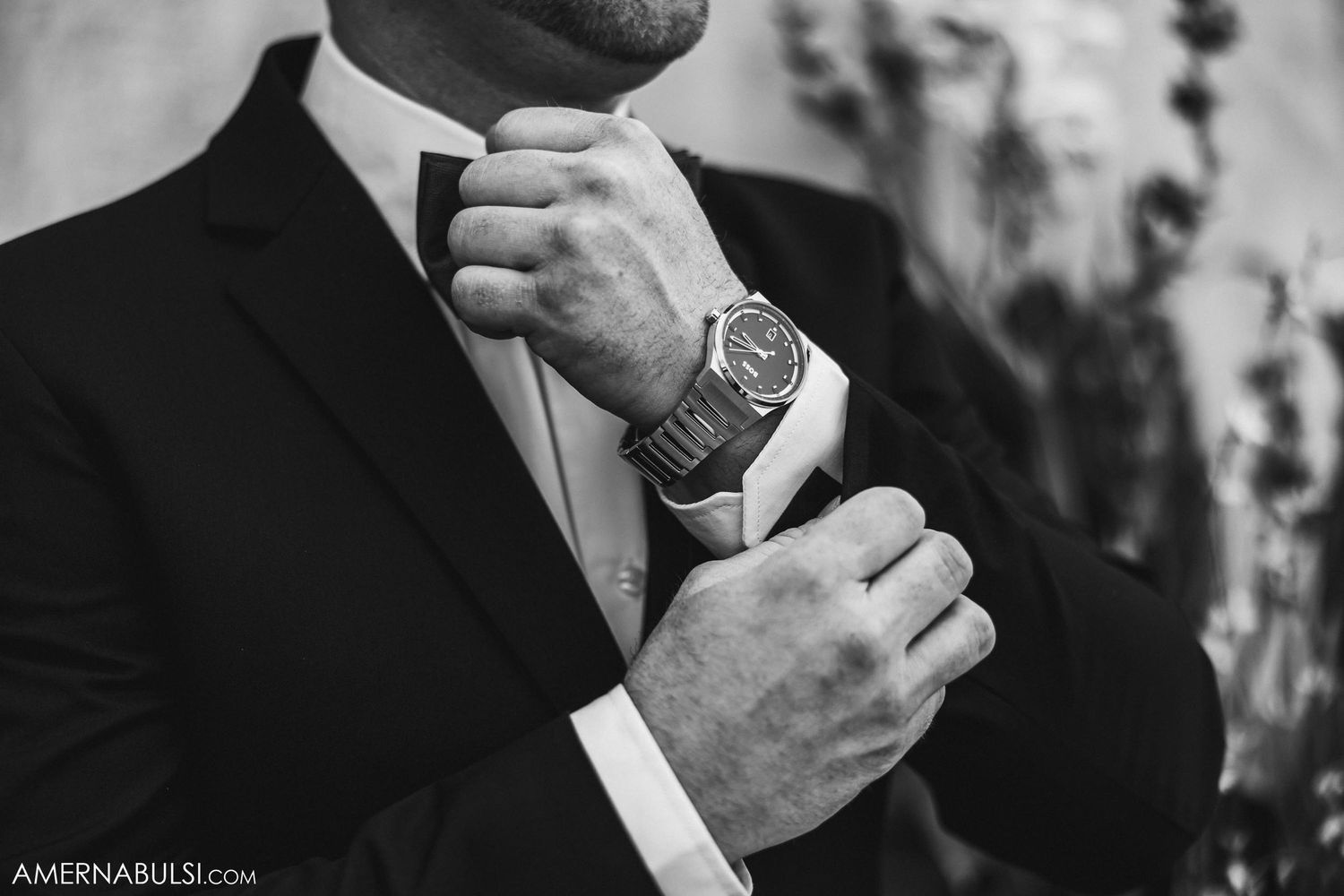 Close-up of groom adjusting tie and watch while wearing formal black suit.