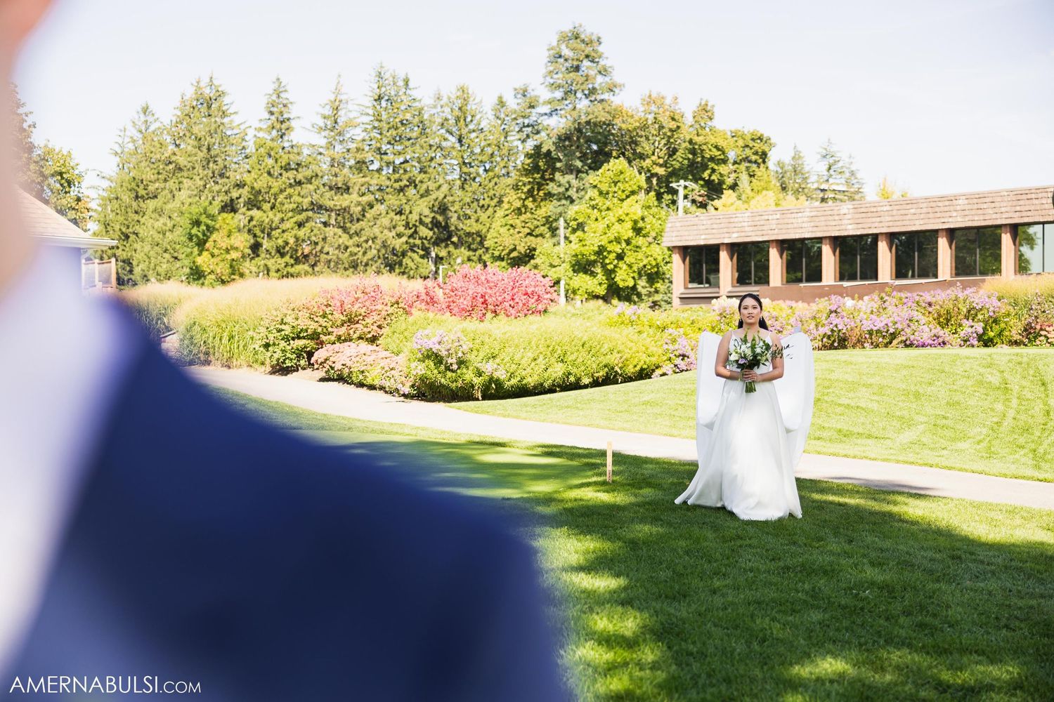 Wedding ceremony first look moment captured on manicured lawn with building in background.