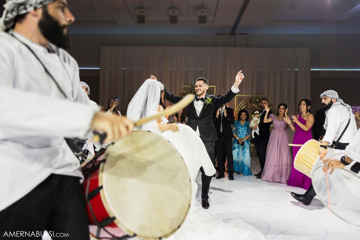 Traditional musicians with drums perform as guests dance during a wedding reception.