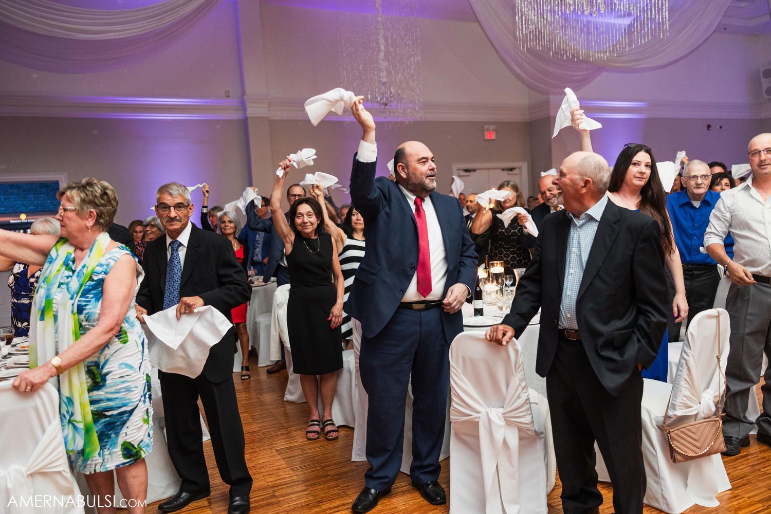 Wedding guests wave napkins in celebration during reception in elegantly decorated ballroom.