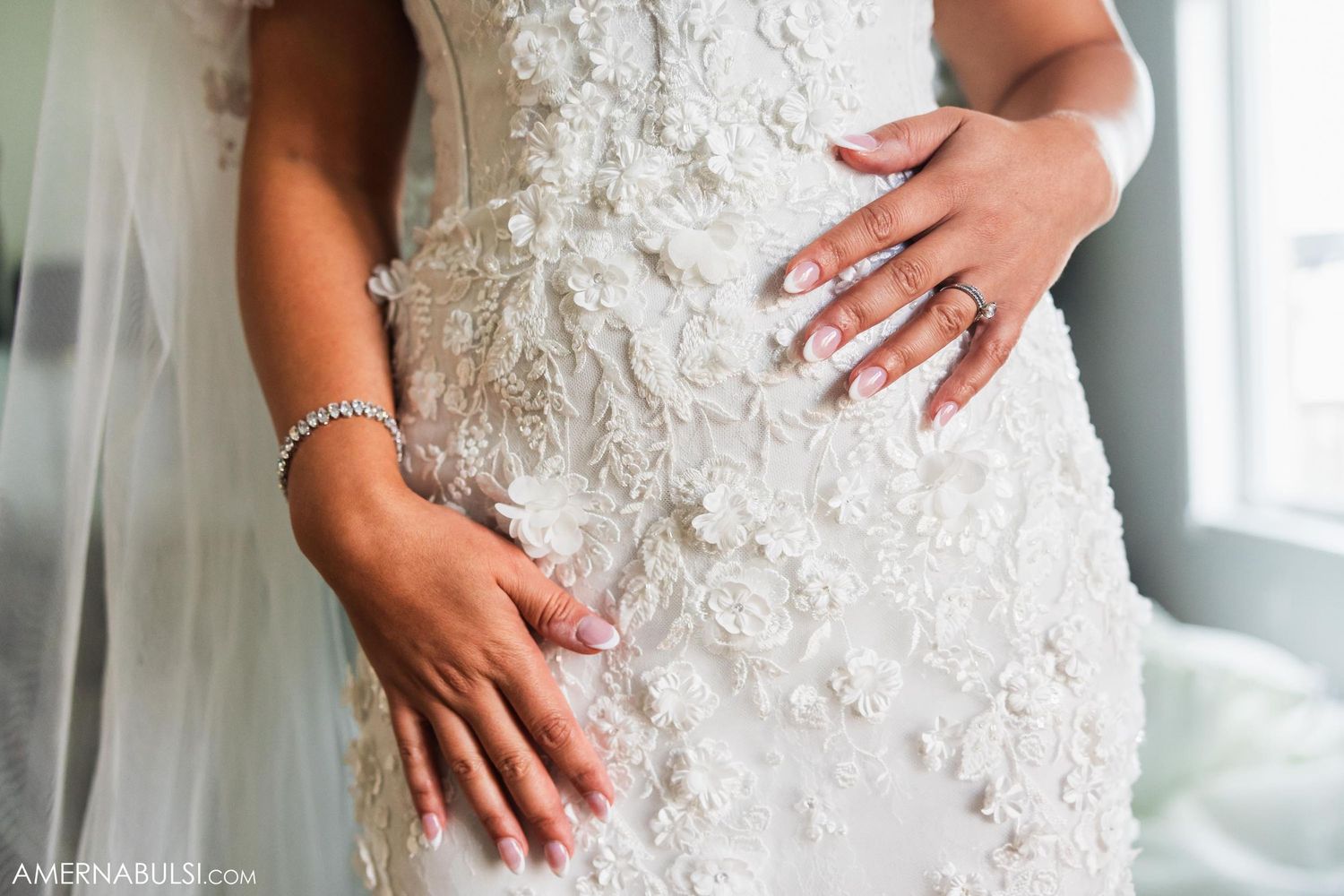 Close-up of hands showing off intricate lace details on a white wedding dress.