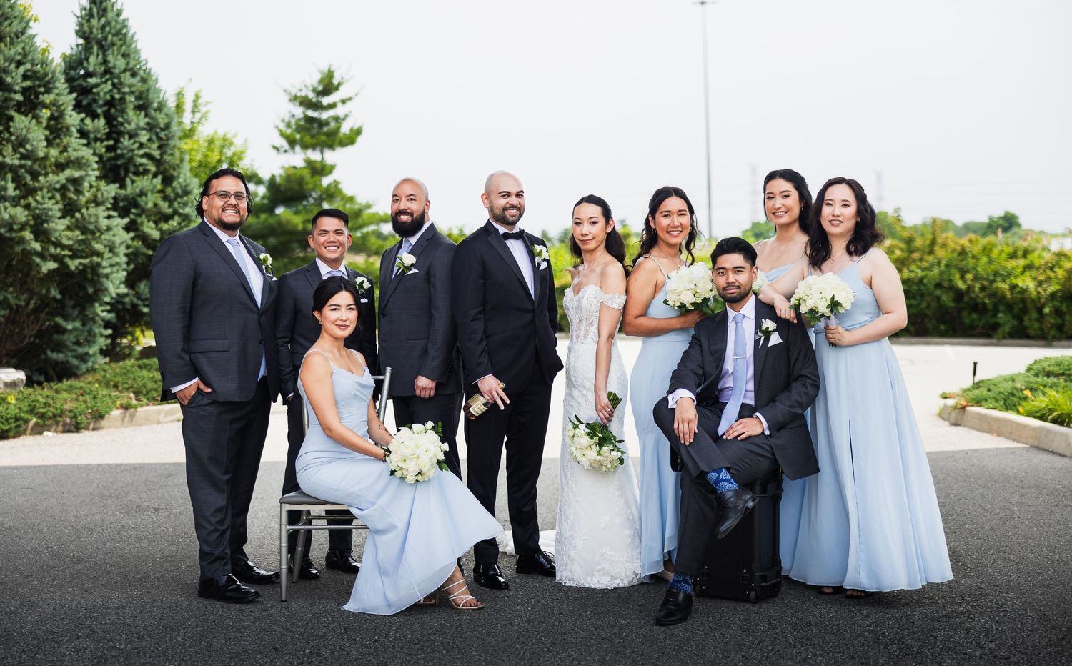 Wedding party poses together outdoors wearing light blue and black formal attire.