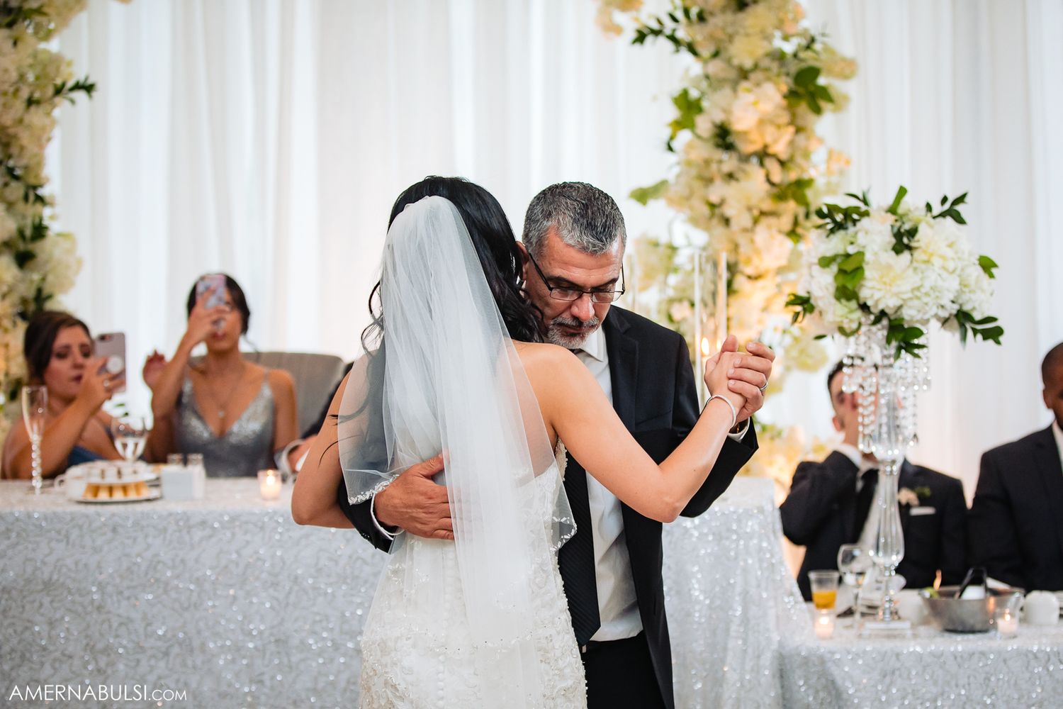 Romantic first dance moment at wedding reception with floral decor and sparkly tablecloth.