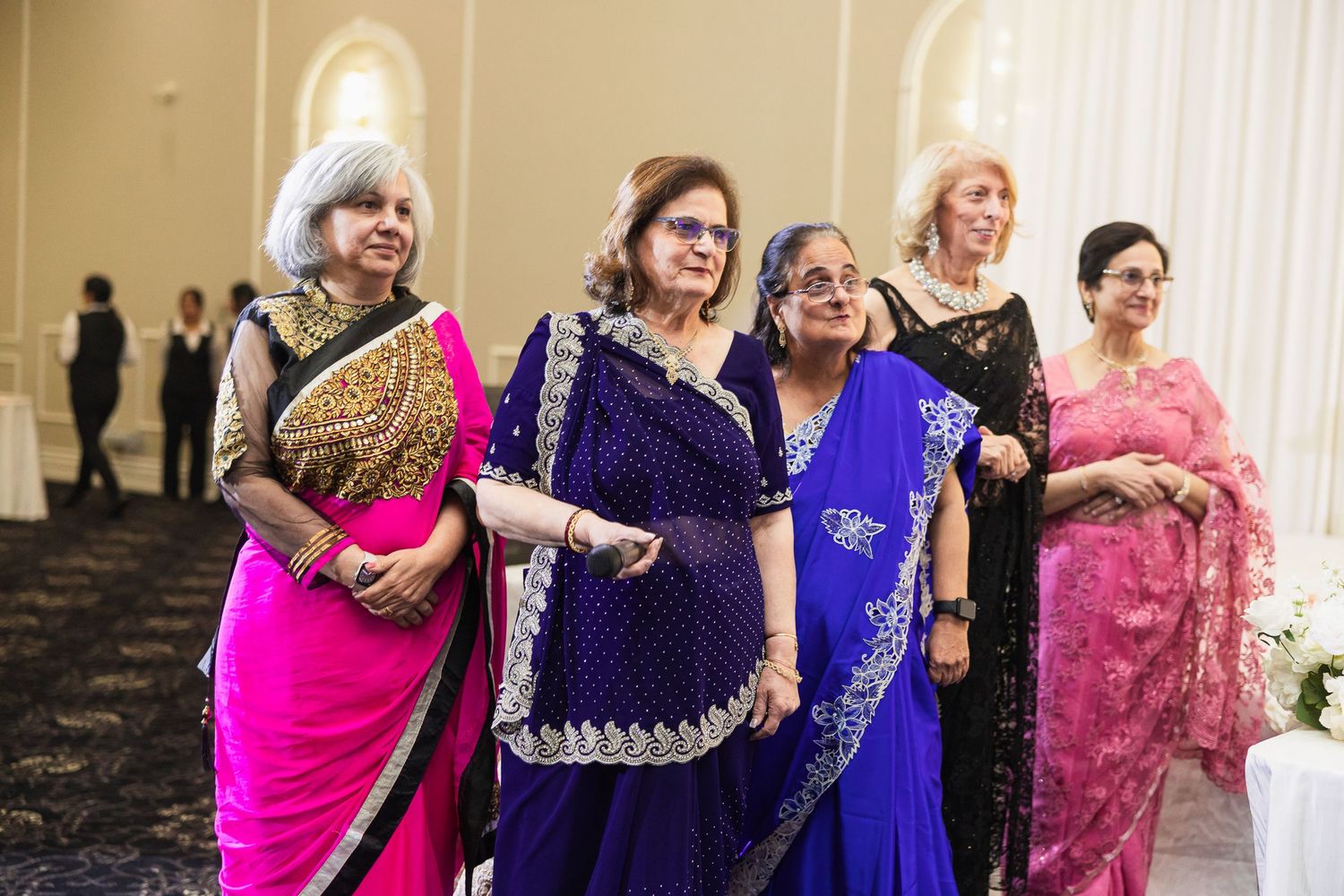 Group of guests in colorful traditional Indian attire dancing together at a wedding celebration.