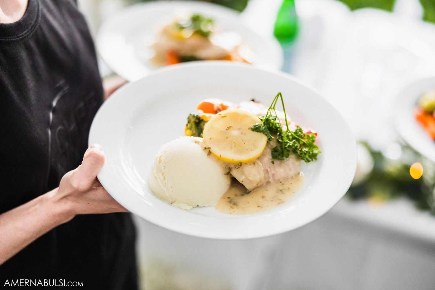 An elegant white plate with seafood and garnish being served at an upscale restaurant.