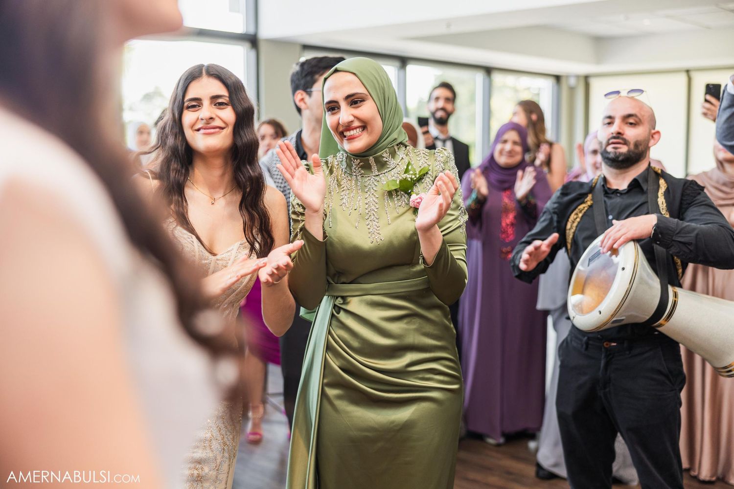 Wedding guests dance and celebrate while musician plays drum in background.
