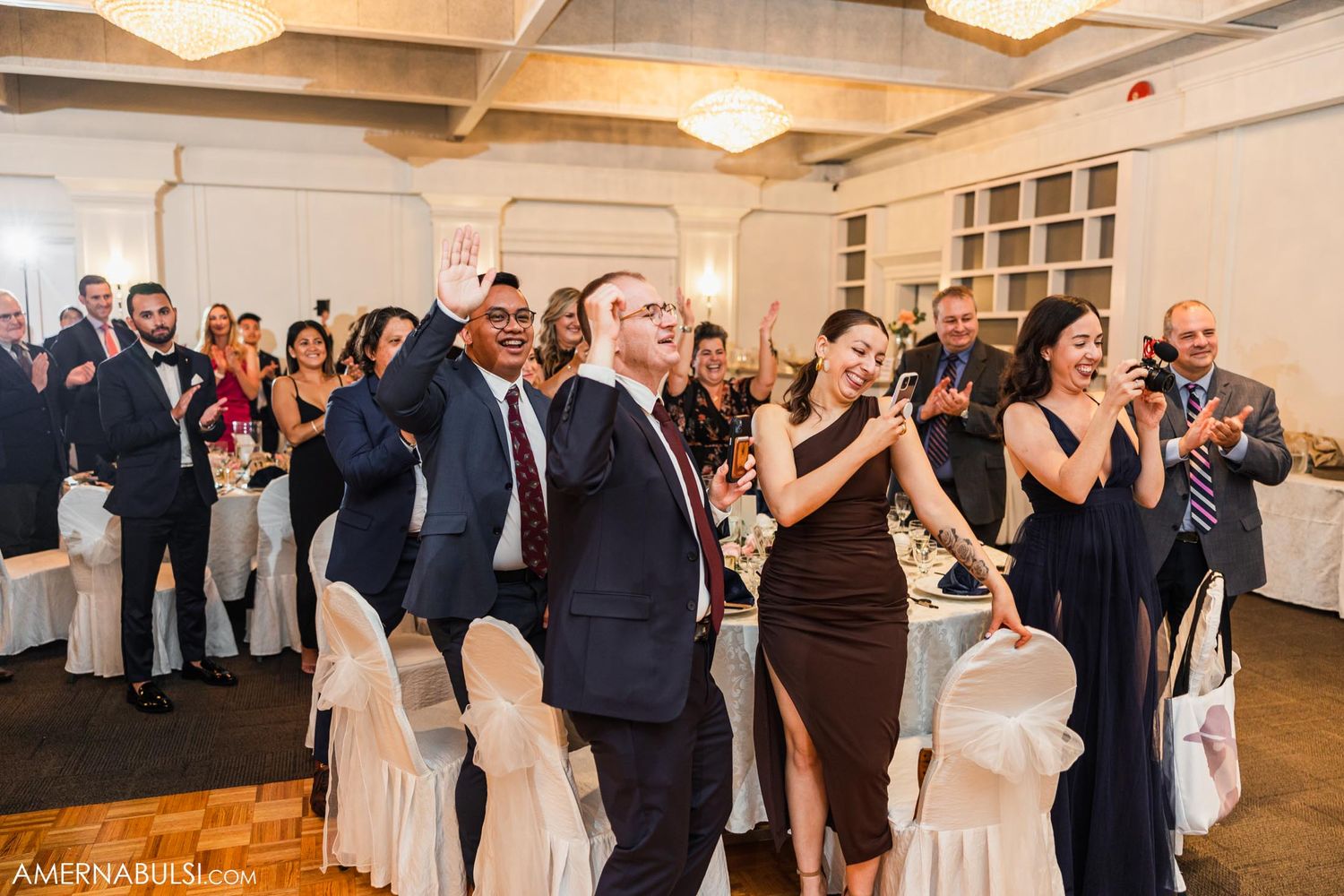 Wedding guests dancing and celebrating on the dance floor at an indoor reception.