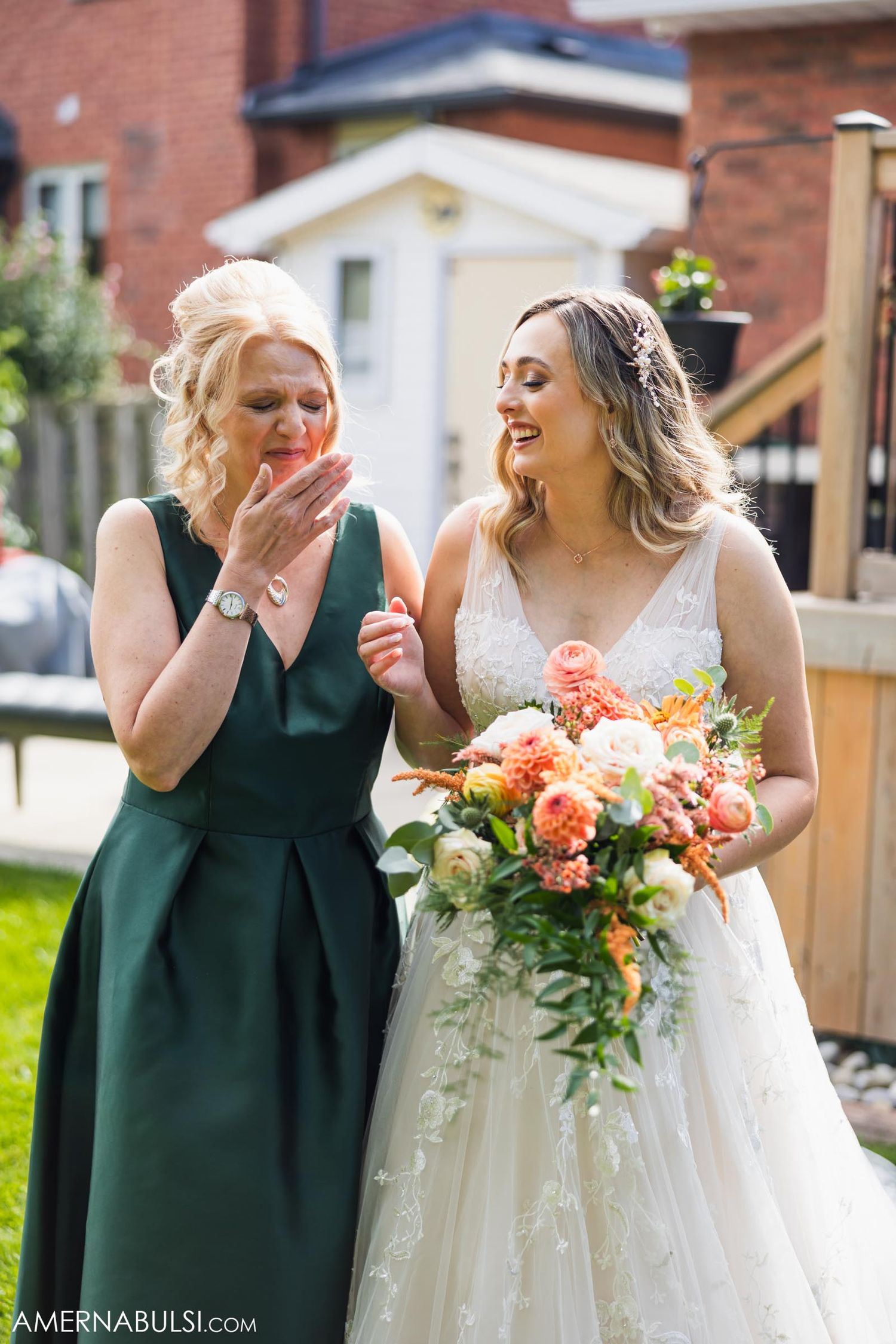 Candid moment of joy shared between two wedding guests with bright floral bouquet.