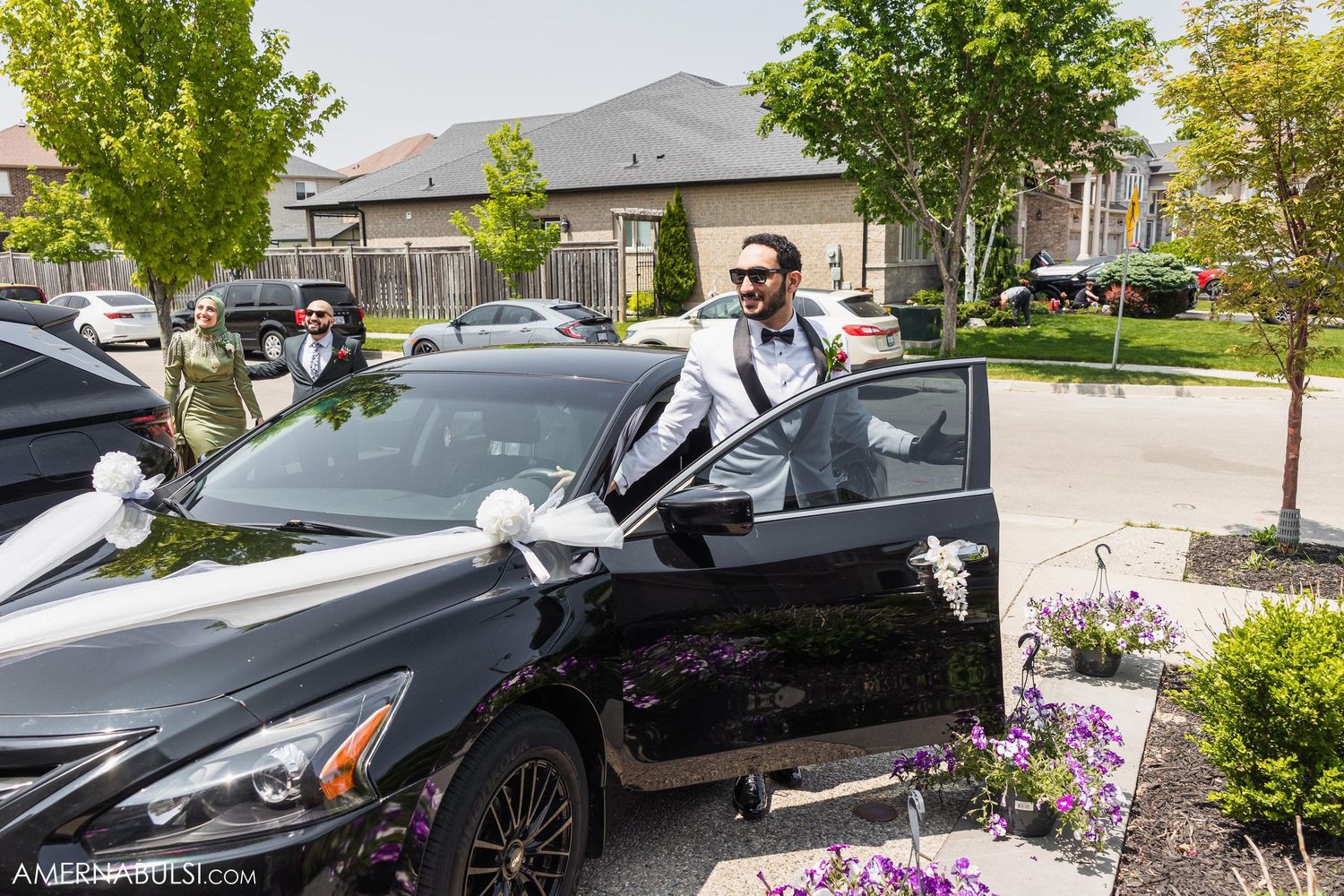 A person in formal attire getting into a decorated black car outside.