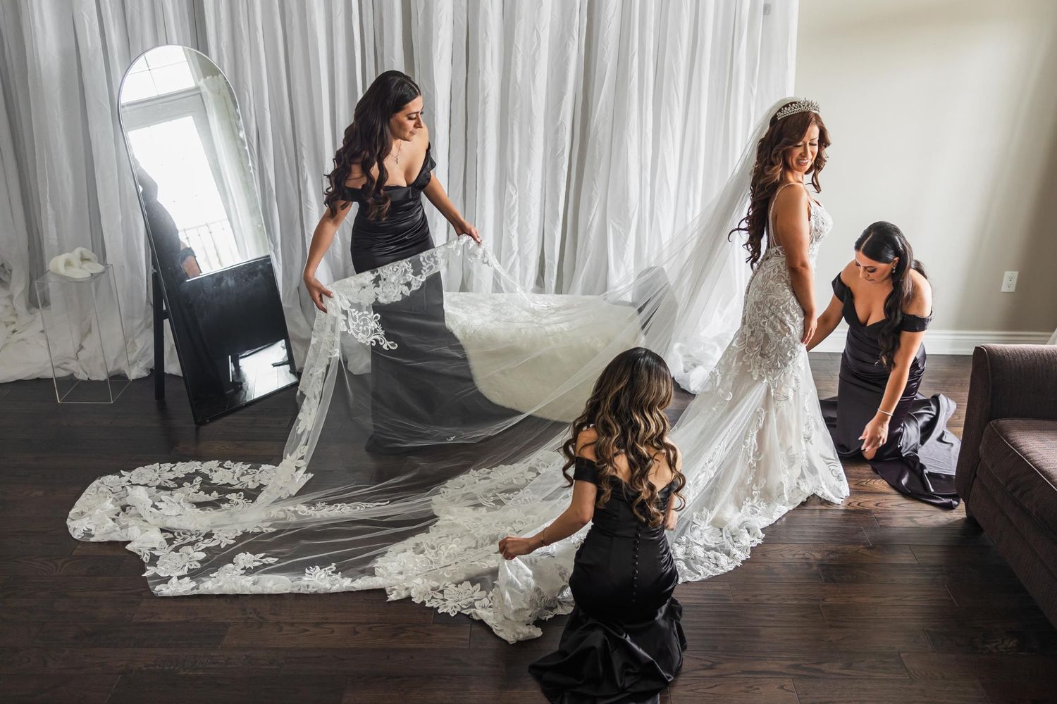Wedding dress preparation scene with bridesmaids helping arrange the intricate lace train.