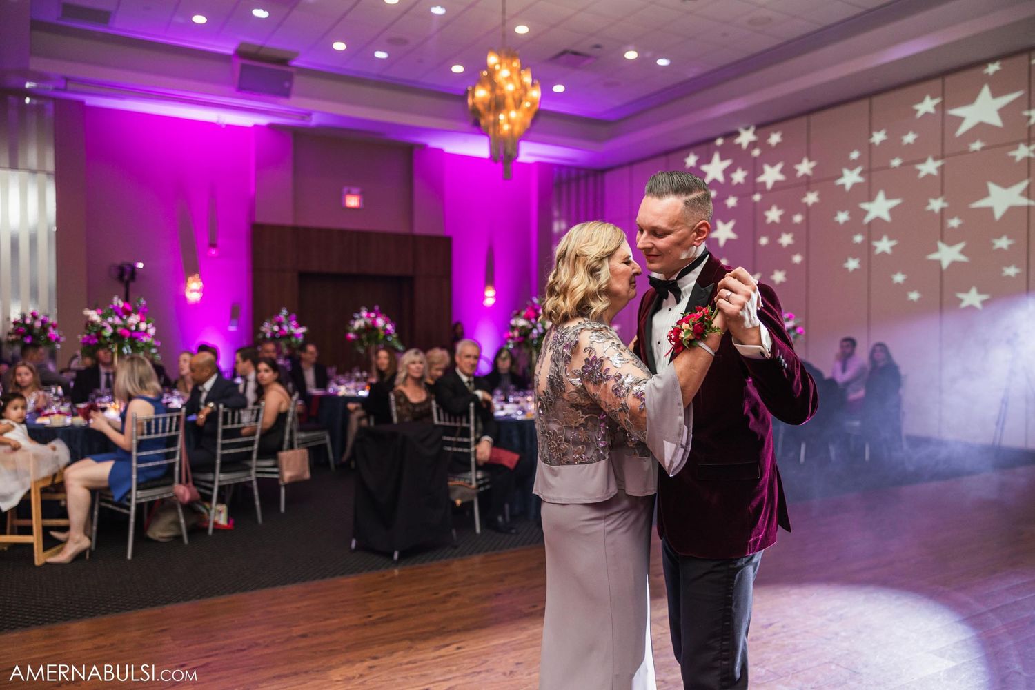 Formal couple dancing in elegant ballroom with purple uplighting and star projections.