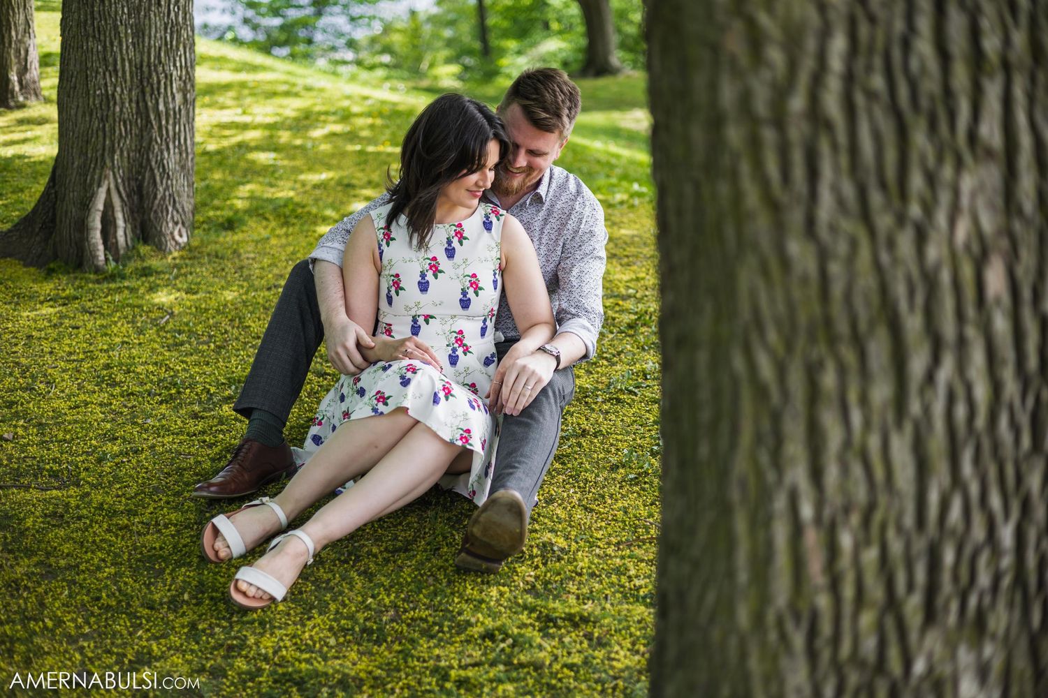 Couple relaxing together on grassy lawn near a tree trunk.