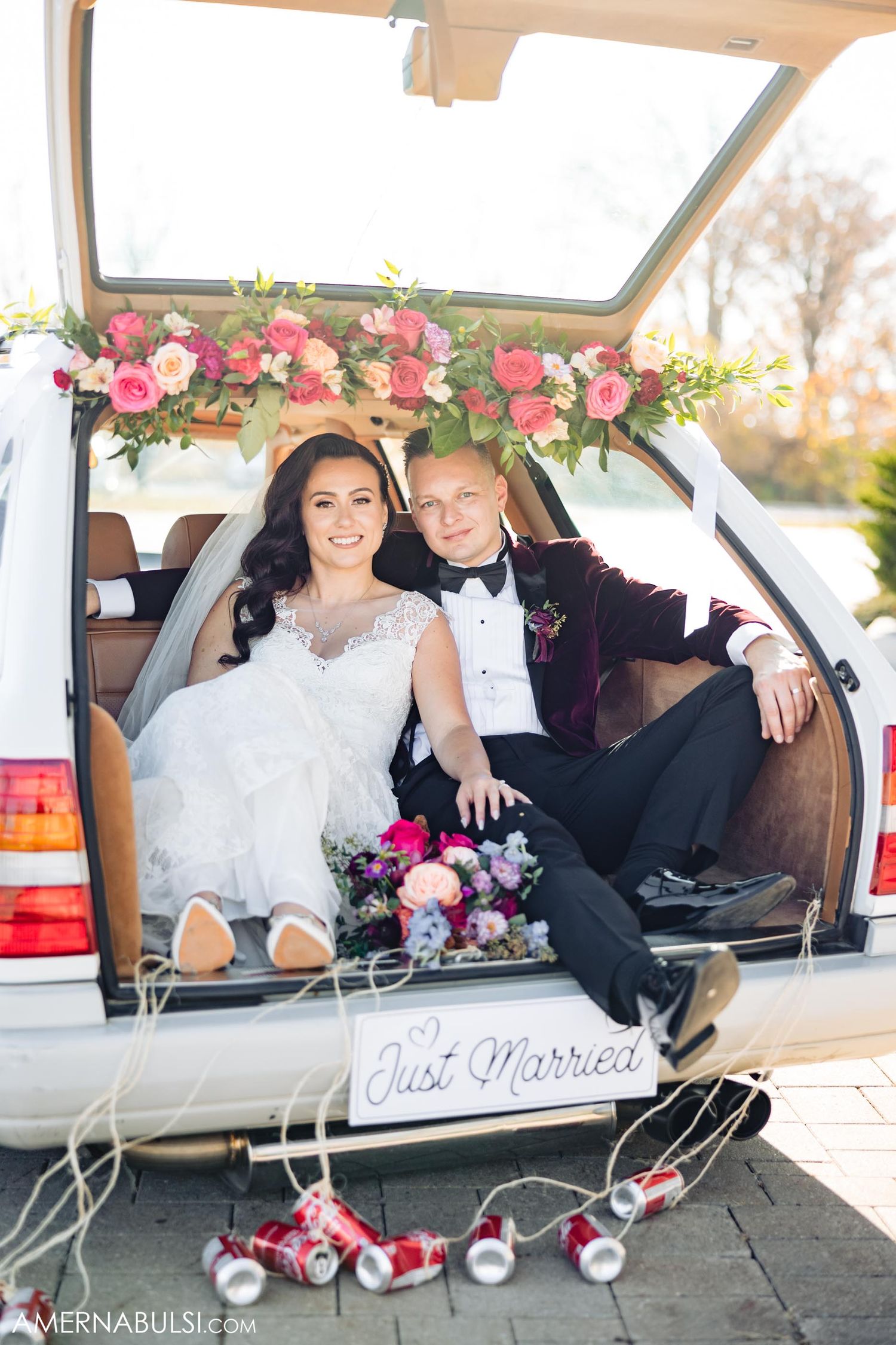 Decorated car trunk with pink floral garland and 'Just Married' sign displays wedding day transportation.