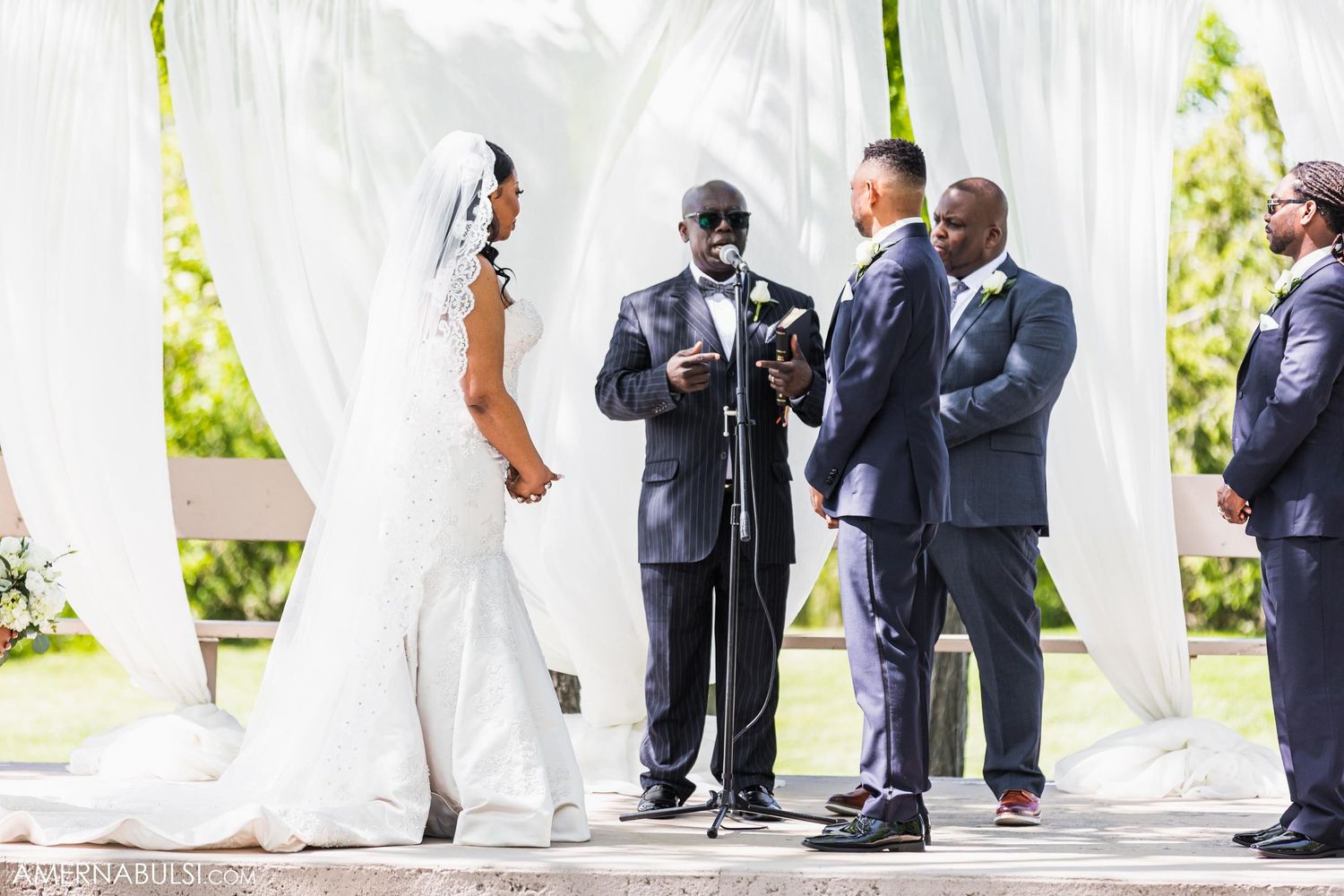 Wedding ceremony in progress under white draping with officiant and wedding party.