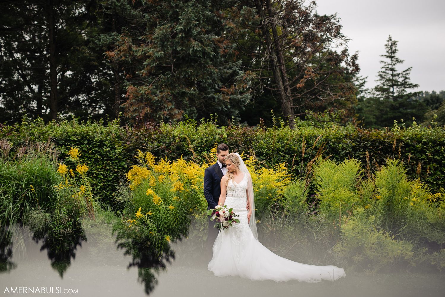 Wedding couple poses in front of lush garden backdrop with yellow wildflowers.