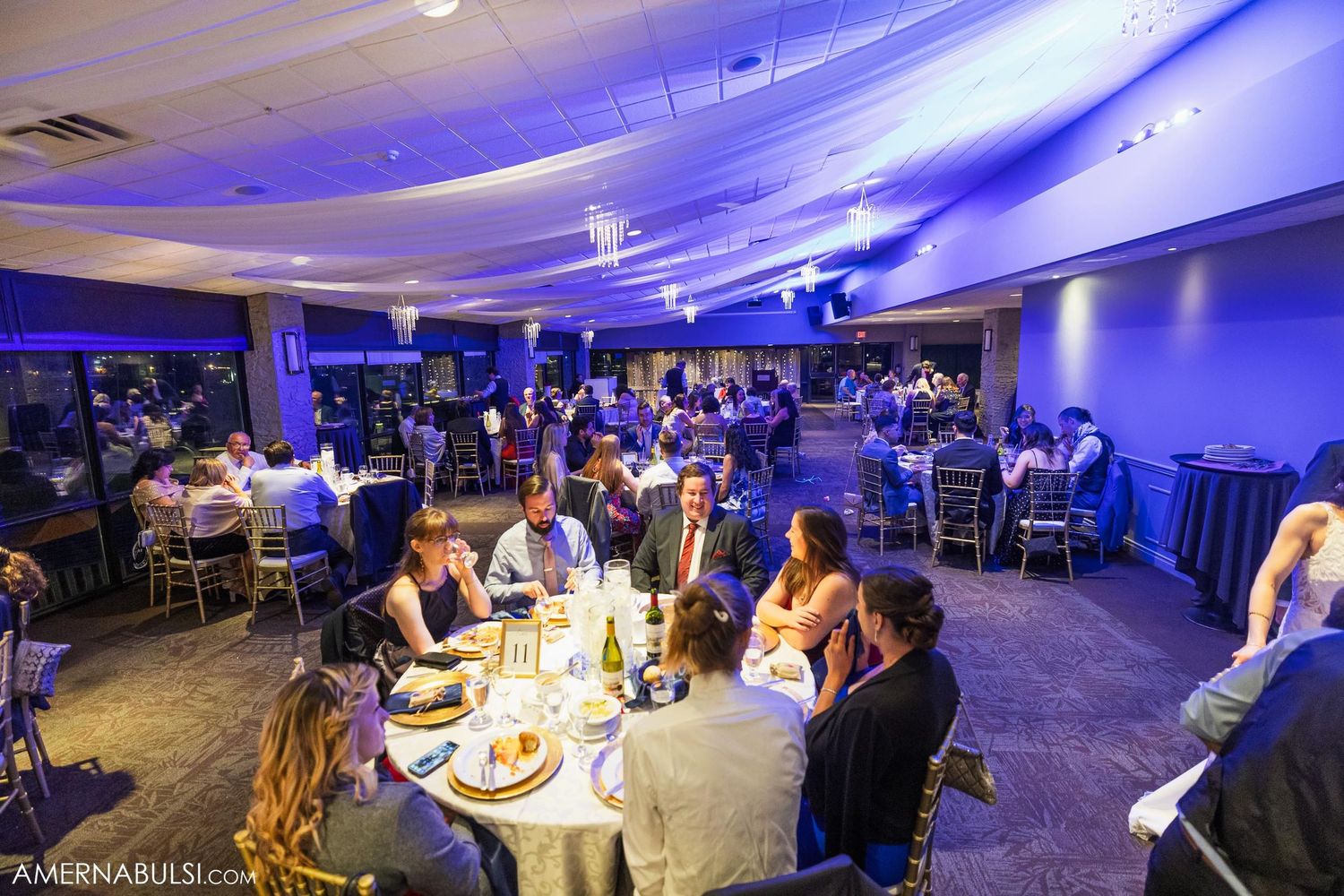 Wedding reception venue with purple uplighting and guests seated at round tables for dinner.