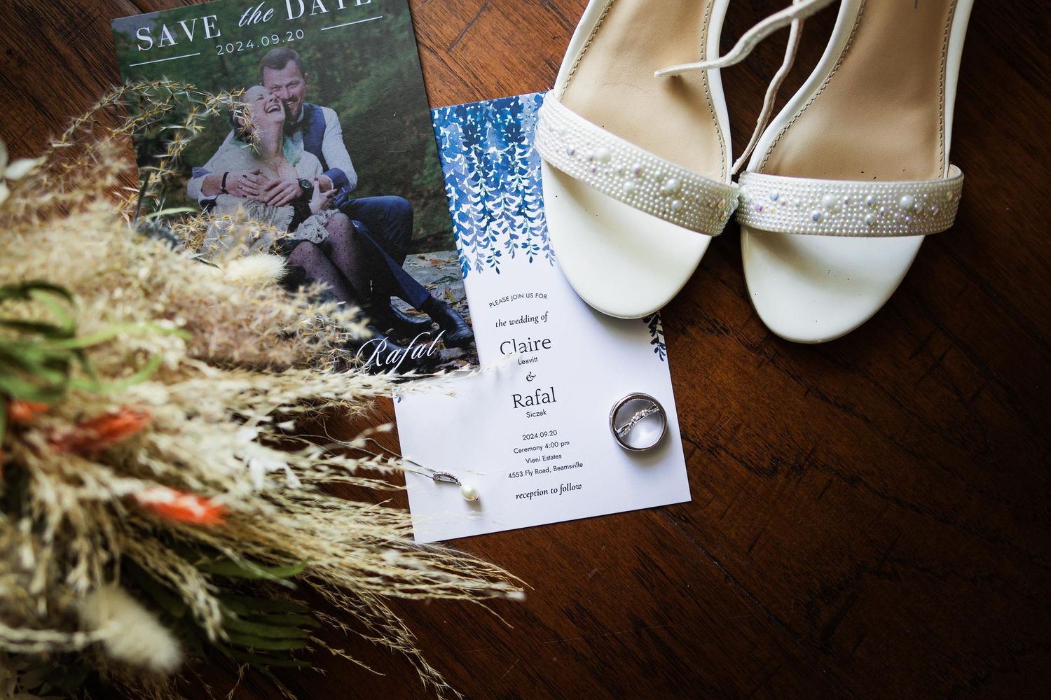 Wedding invitation with dried flowers and sparkly bridal shoes on wooden surface.