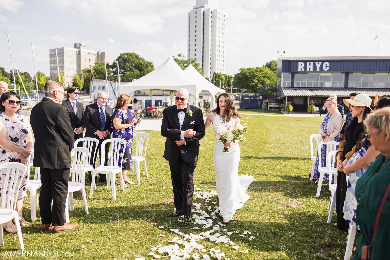 A wedding processional on a lawn with rose petals scattered along the aisle.