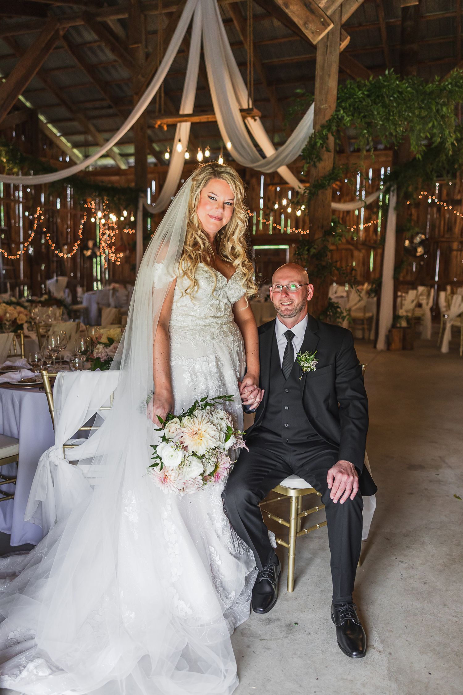 Newlyweds share joyful moments while resting on vintage couches in a rustic barn wedding venue adorned with elegant decor.