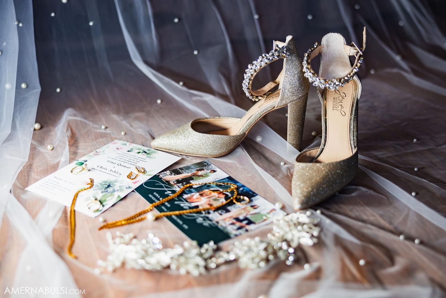 Wedding accessories including sparkly heels and invitation cards arranged on tulle fabric.