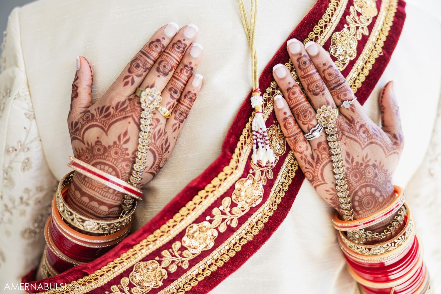 Detailed view of henna-adorned hands with red and gold wedding bangles and traditional attire.