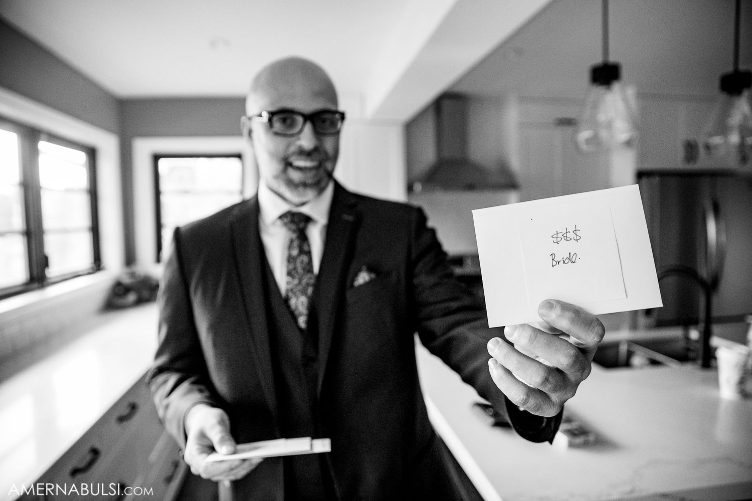 A person in a dark suit holds up a handwritten note in a modern kitchen setting.