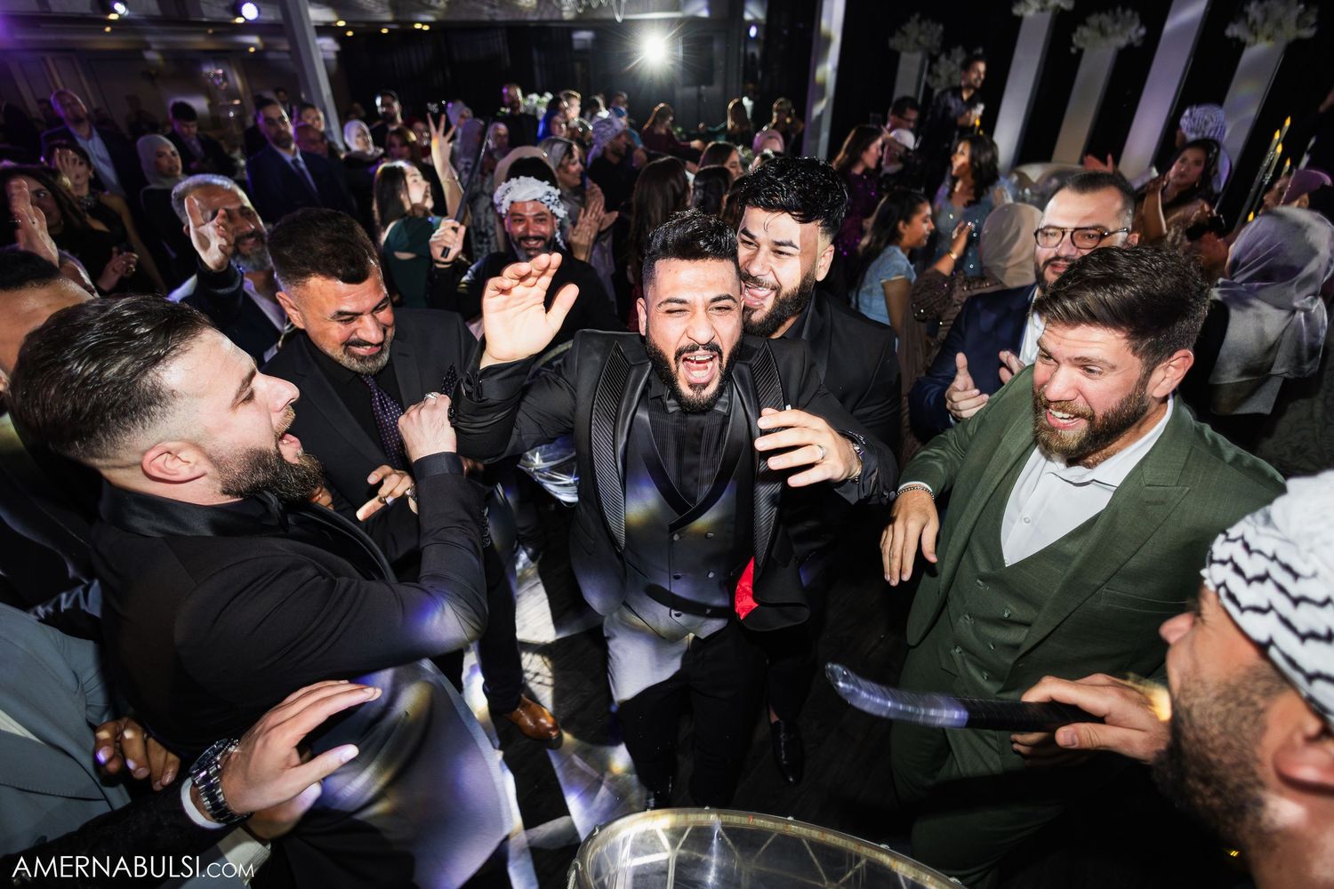 Partygoers dance enthusiastically under purple spotlights at a festive wedding reception.